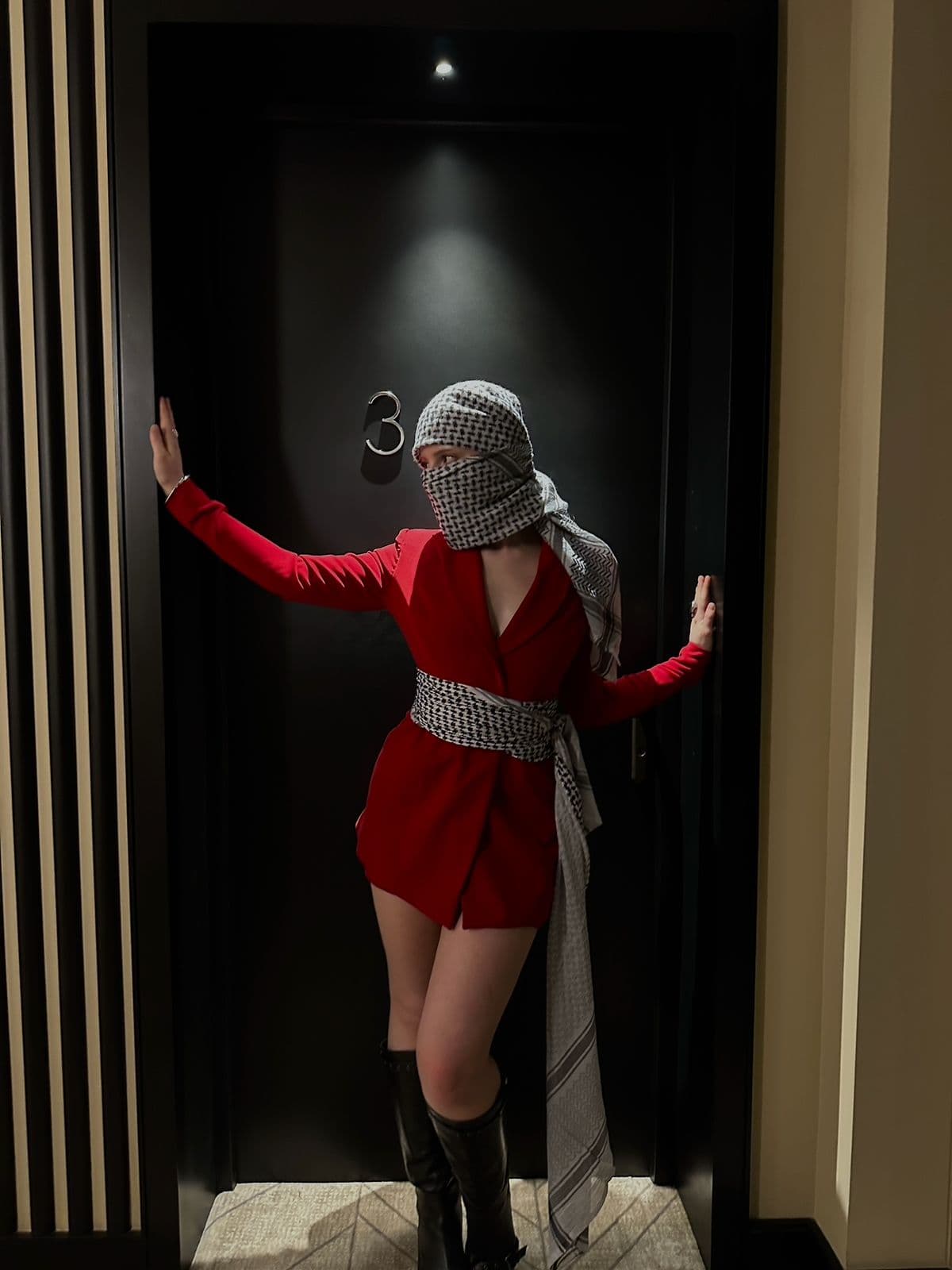 Atelier Qeblawi — Crimson Tailoring — model in red blazer-dress and kufiyeh wrap, dark hotel doorway, Palestine debut collection