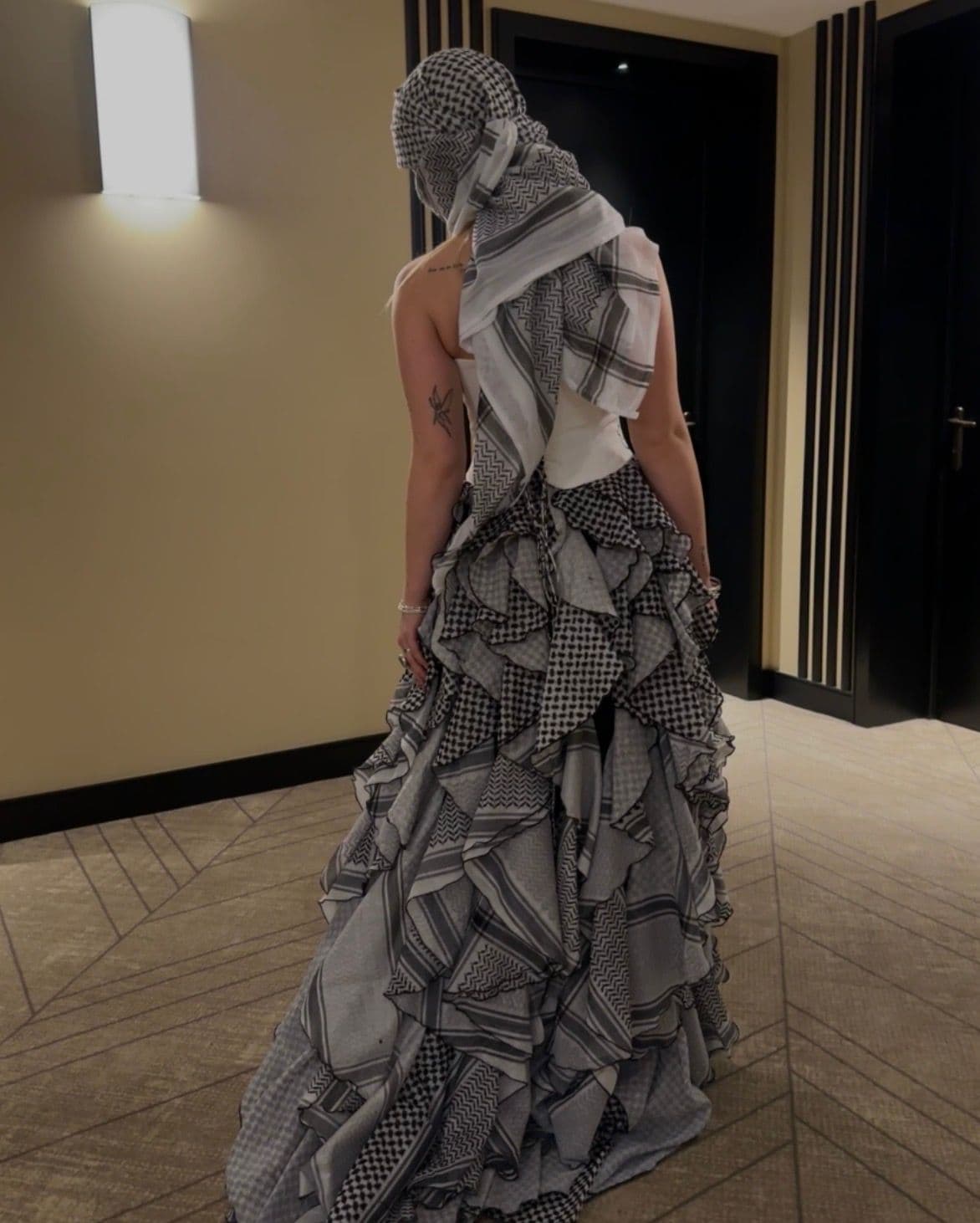 Atelier Qeblawi Calligraphy Gown — three-quarter back view of the layered kufiyeh-fabric ruffle gown in a hotel hallway.