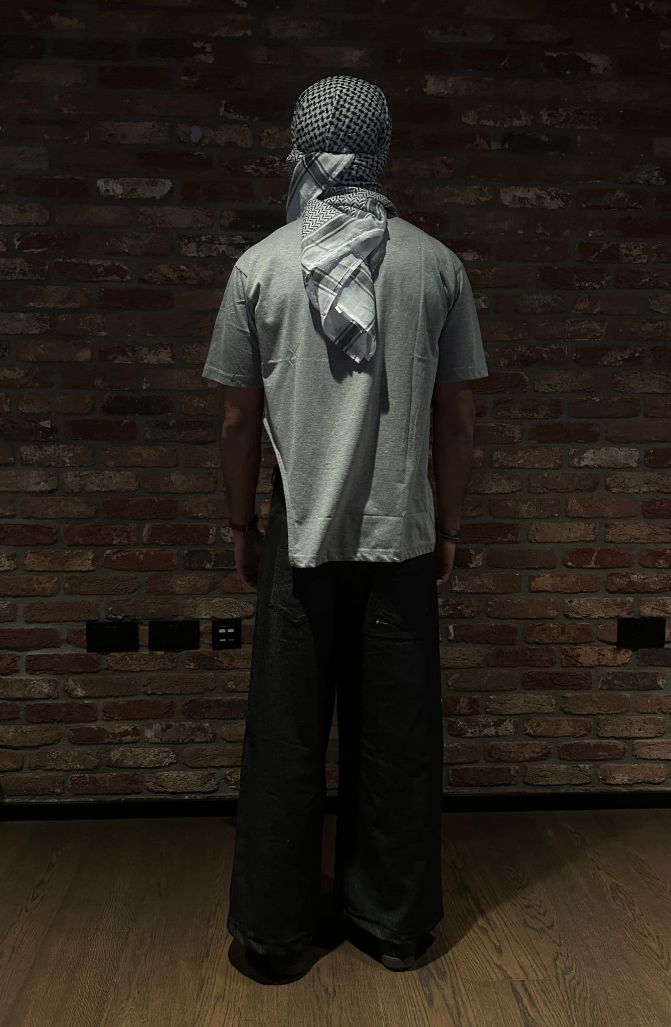 Atelier Qeblawi Painted Streetwear — back view of the same grey t-shirt and wide-leg dark denim, kufiyeh head and shoulder wrap.