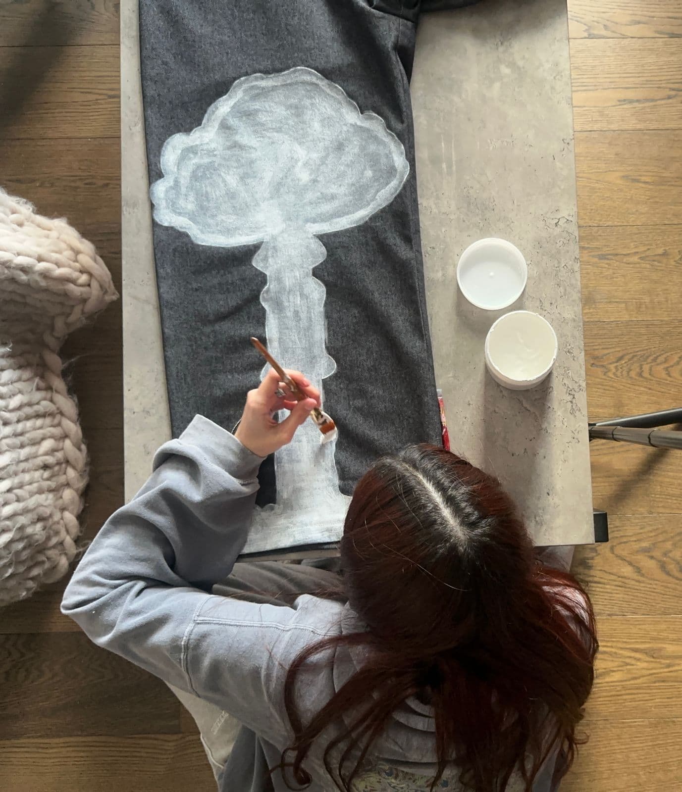 Rhea Qeblawi hand-painting a fabric panel — a cloud-like form on dark grey wool.